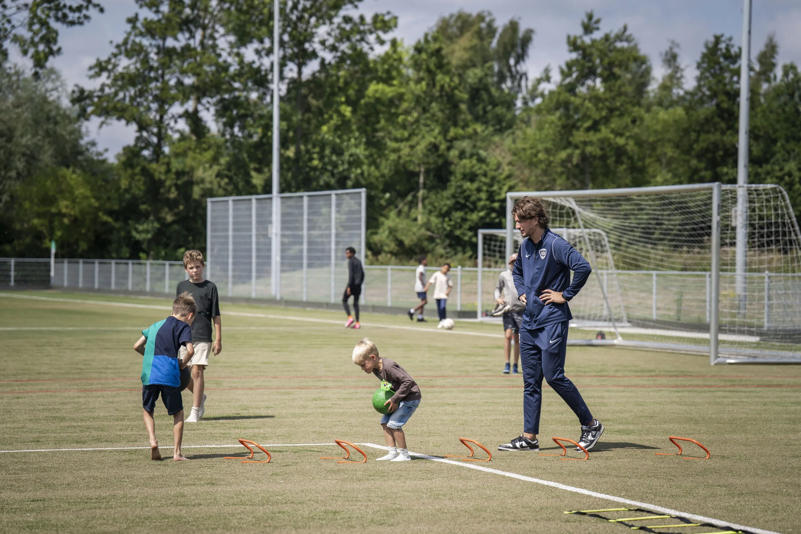 Trainer en een aantal kinderen die hij over kleine obstakels laat springen