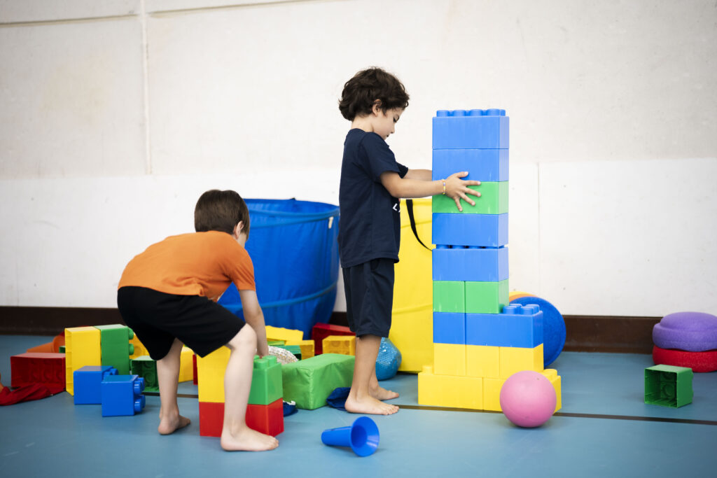 Peuters in een gymzaal die met blokken, een bal en pionnen aan het bouwen en spelen zijn