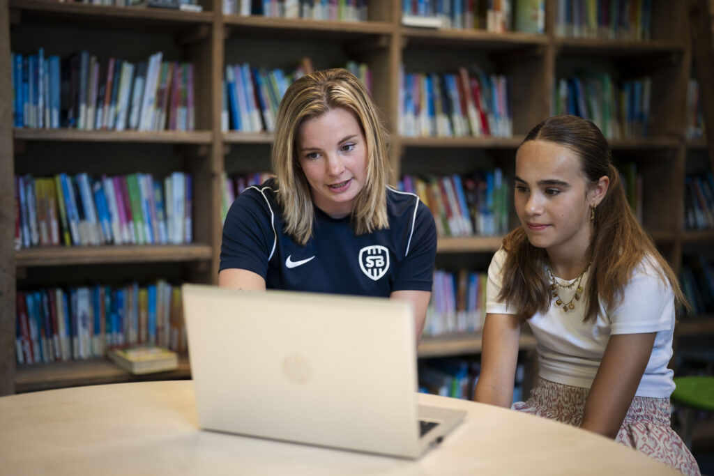 Trainster legt iets uit op de laptop aan een scholiere