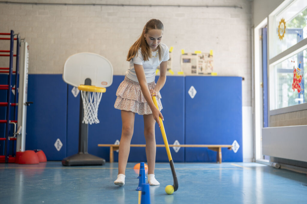 Jonge meid die met een hockeystick de bal door de pionnen begeleidt